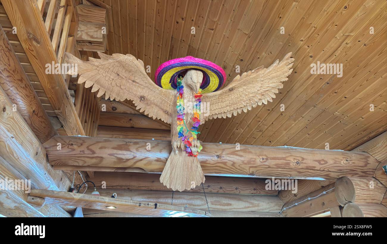 Scultura in legno di un'aquila decorata con fiori da festa e cappello. Appeso a un tetto di legno. Decorazione per le feste. Bar APRS-skimountain. Piemonte - Immagine stock catturata con smartphone