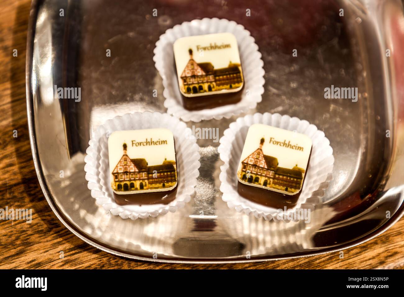 Tre praline stampate con un motivo del municipio di Forchheim si trovano in involucri di carta bianca su un vassoio d'argento. Il municipio tardo-medievale, con il suo frontone a gradoni in legno a graticcio, fu costruito nel 1402. Paradeplatz, Forchheim, Bavaria, Germania. Foto Stock