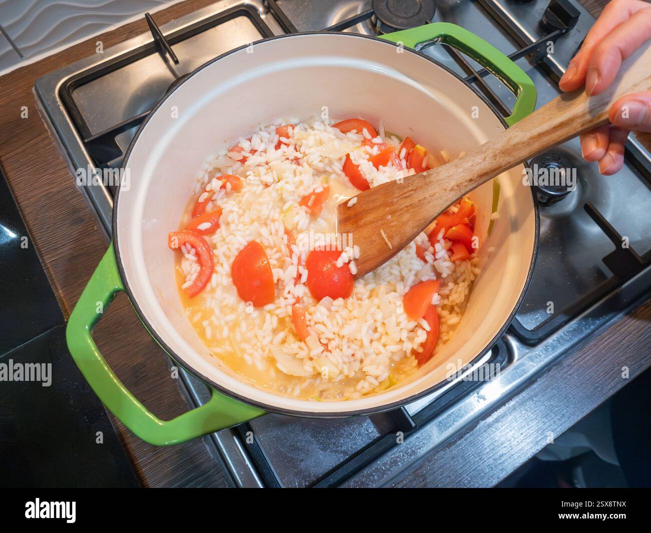 Un uomo che cucina il riso risotto in una pentola grande su un piano cottura a gas, mescolando il riso per assicurarsi che assorba l'acqua e non bruci, Regno Unito. Concetto: Cucina casalinga Foto Stock