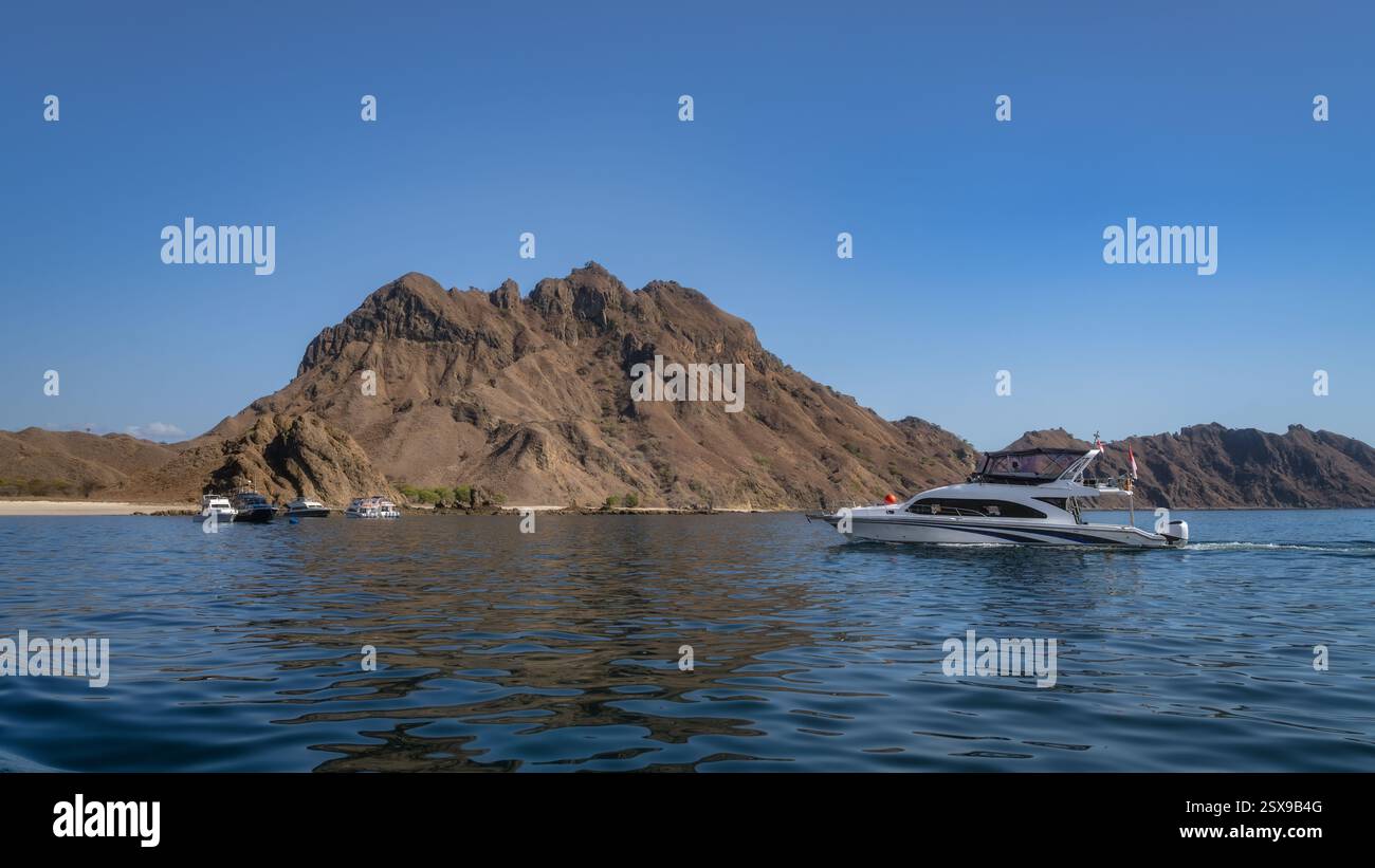 Una pittoresca scena costiera con lussuosi yacht ancorati vicino a un'isola rocciosa sotto un cielo blu limpido, perfetto per l'esplorazione marittima e il relax Foto Stock