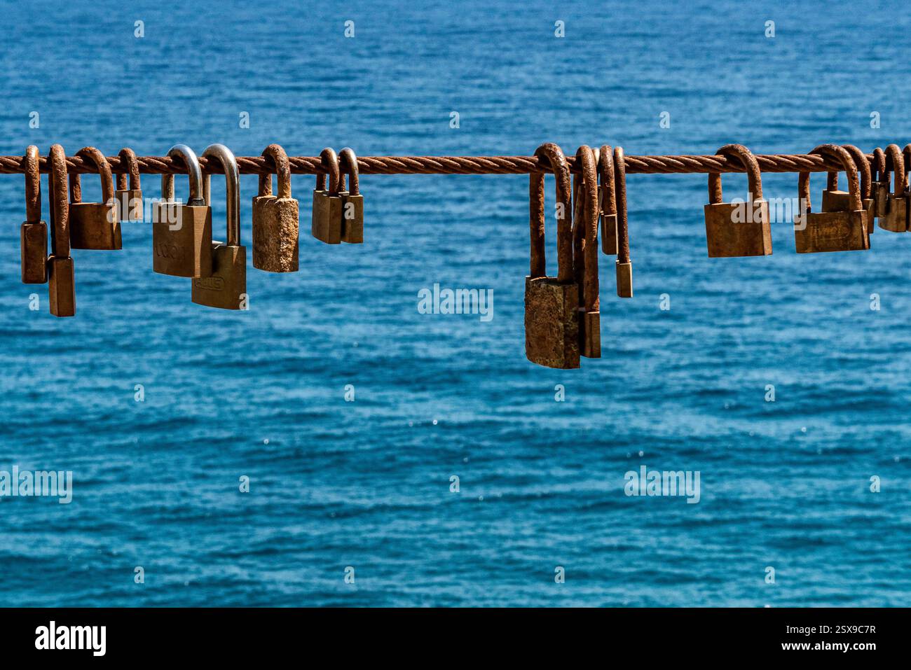 Lucchetti d'amore rustici appesi su una recinzione sul mare contro l'oceano azzurro, simboleggiano l'amore e l'impegno eterni sulla costa mediterranea Foto Stock