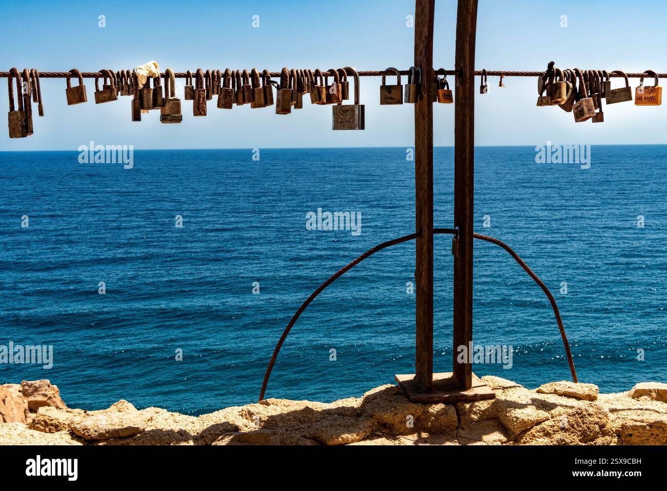 Lucchetti d'amore rustici appesi su una recinzione sul mare contro l'oceano azzurro, simboleggiano l'amore e l'impegno eterni sulla costa mediterranea Foto Stock