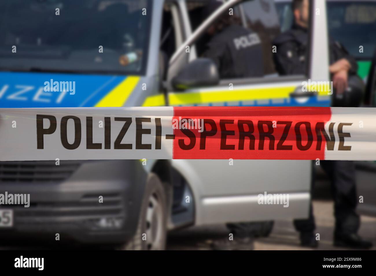 (Fotomontaggio) immagine simbolo di un'operazione di polizia: Nastro barriera con la scritta POLIZEI SPERRZONE davanti a un veicolo di emergenza Foto Stock (Fotomontaggio) immagine simbolo di un'operazione di polizia: Nastro barriera con la scritta POLIZEI SPERRZONE davanti a un veicolo di emergenza Foto Stock