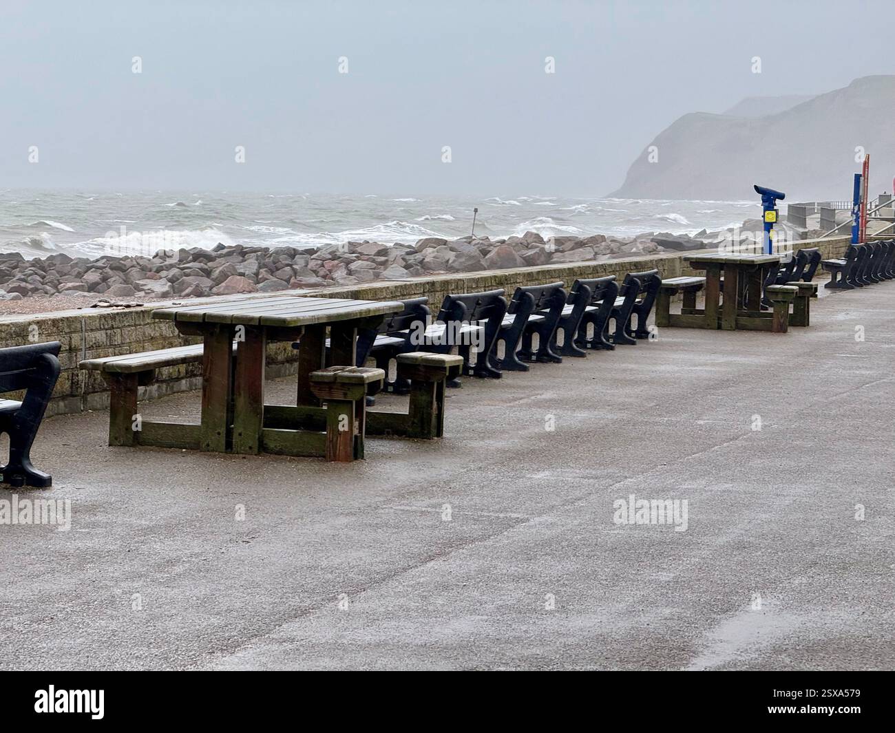 Tavolo, sedie e panchine deserti sul fronte mare della baia occidentale in un giorno di tempesta - Immagine stock catturata con smartphone