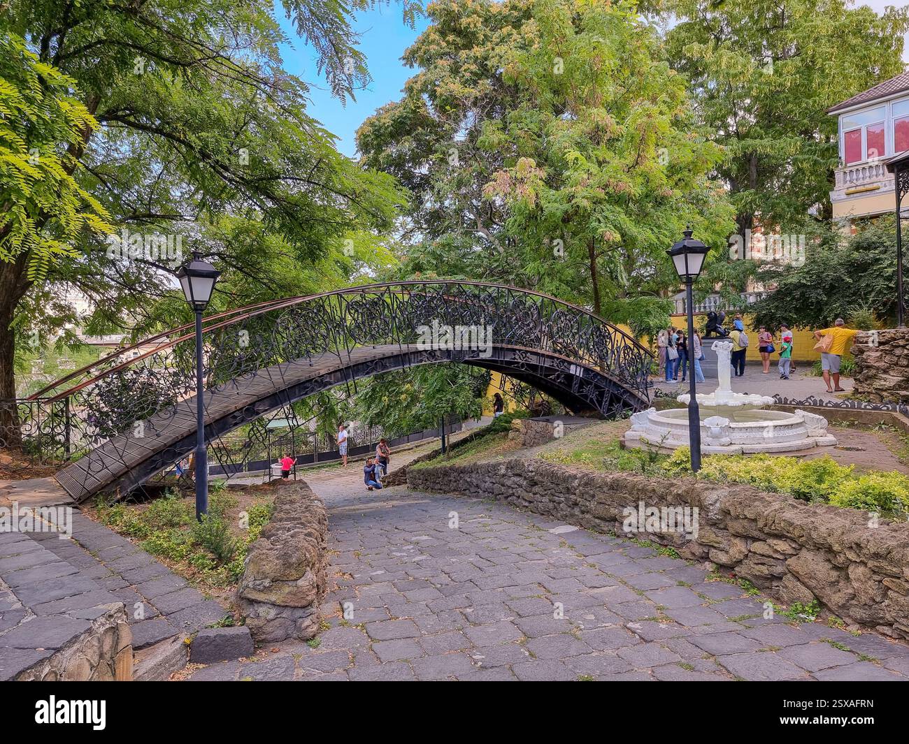 Piccola passerella in metallo e fontana con scultura nell'angolo della Vecchia Odesa / Odessa, un piccolo museo all'aperto vicino al Ponte Tioschin - Immagine stock catturata con smartphone