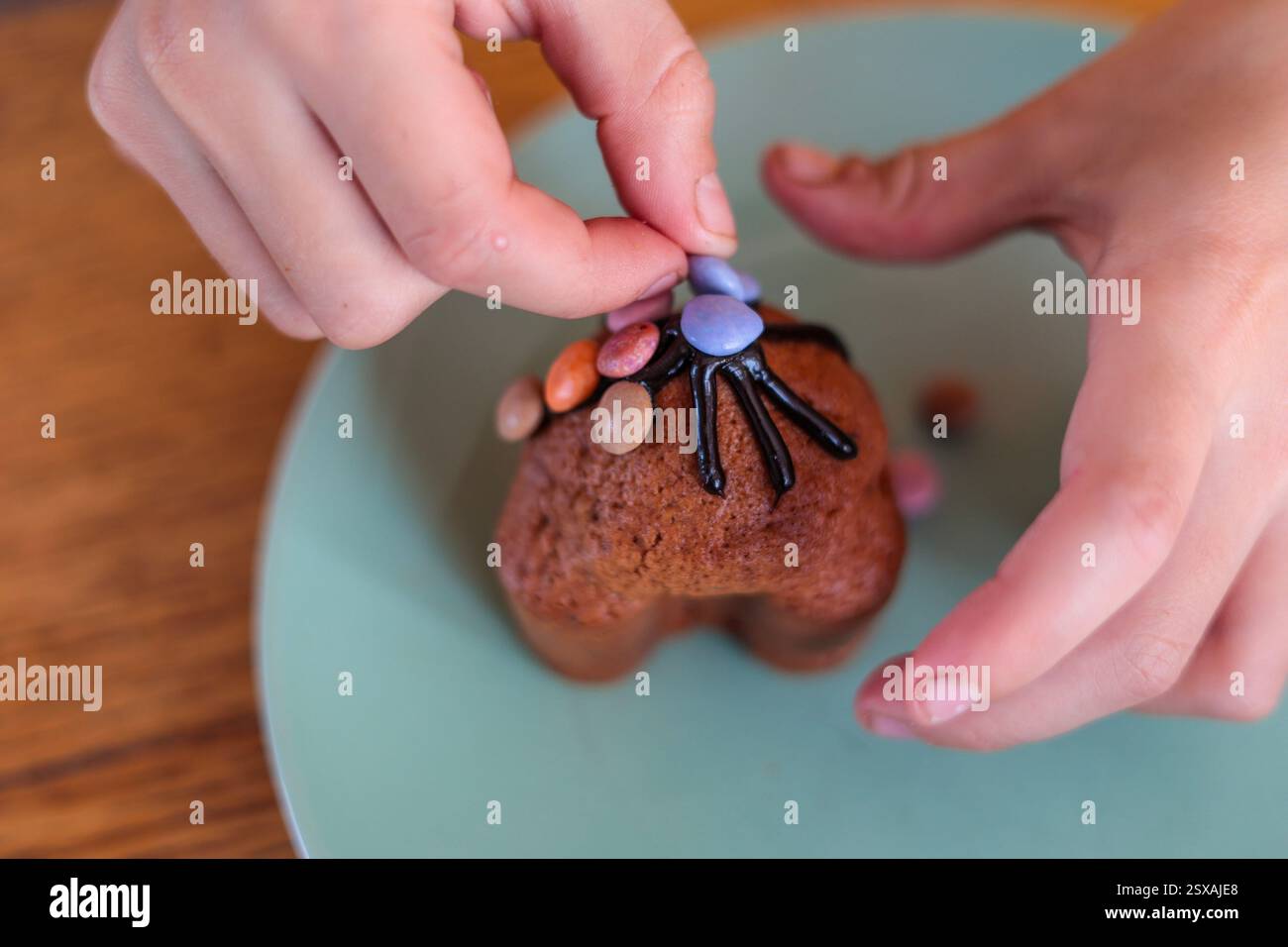 Le mani dei bambini decorano la glassa di cioccolato di un cupcake pasquale con caramelle viola Foto Stock