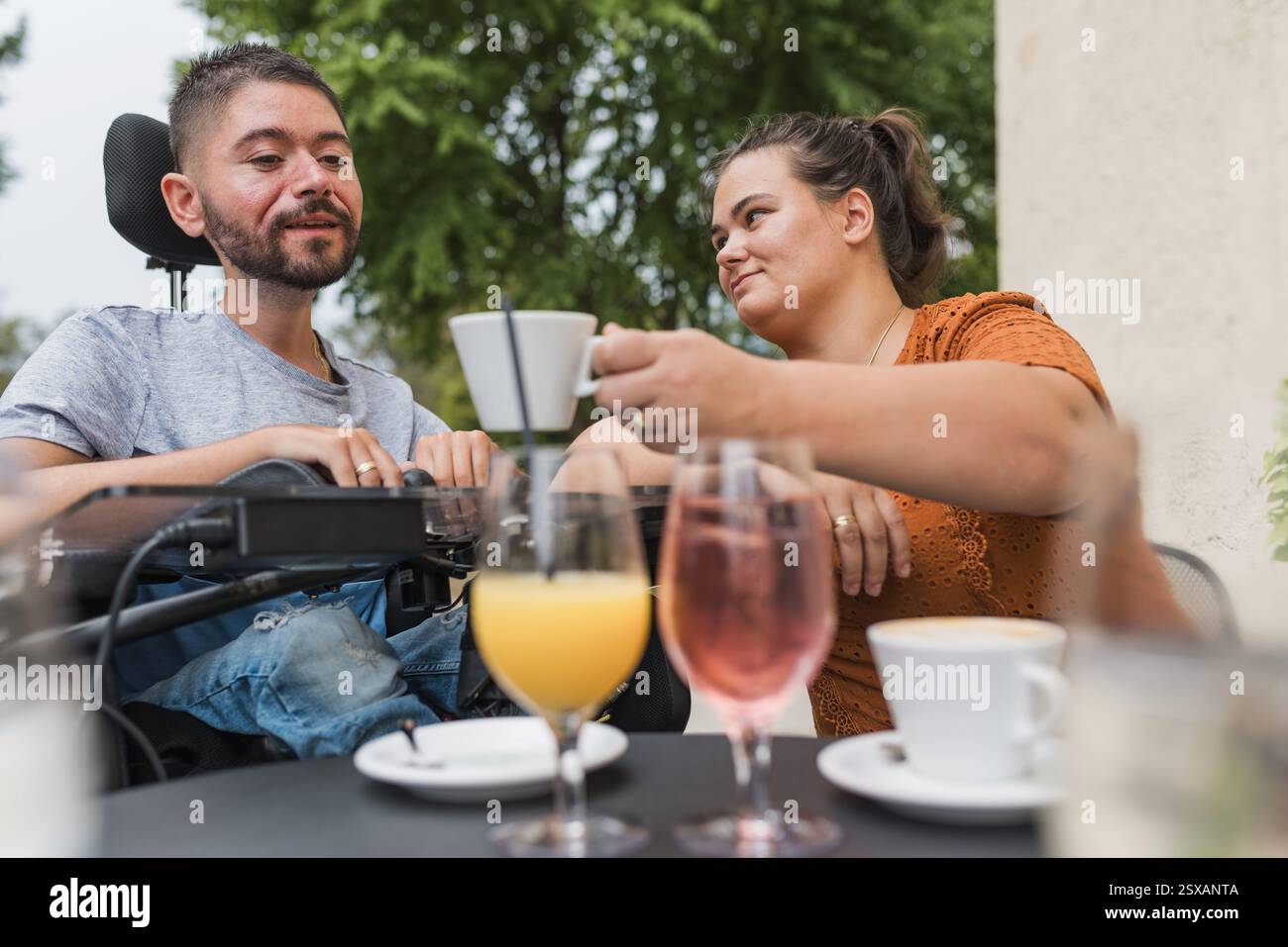 Ragazza che assiste il suo ragazzo con disabilità fisica bevendo caffè in un bar. Amore e conquista di concetti di avversità. Foto Stock