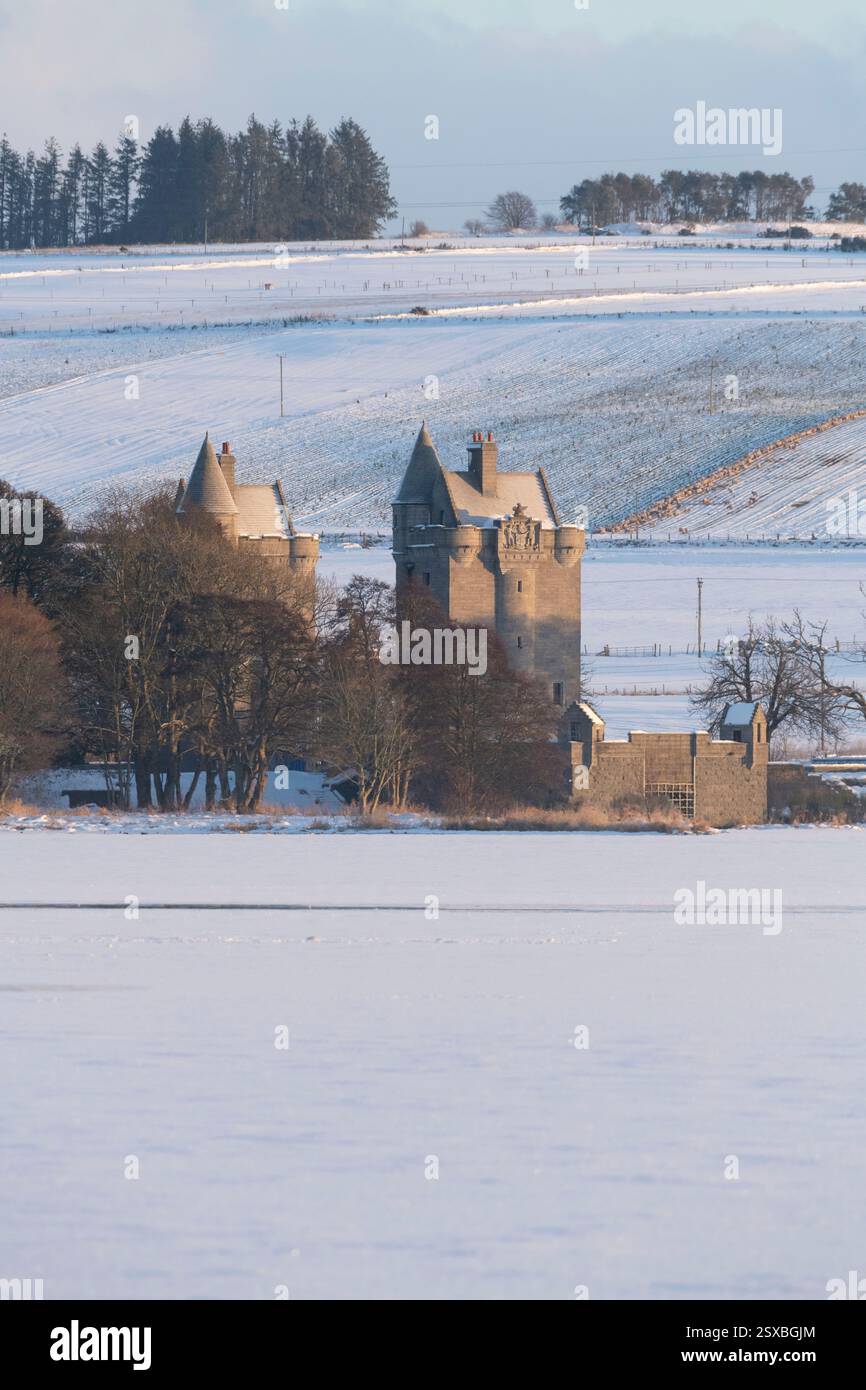 Le Gatehouse Towers a Dunecht Estate si vedono attraverso il lago ghiacciato e coperto di neve di Skene in inverno Foto Stock