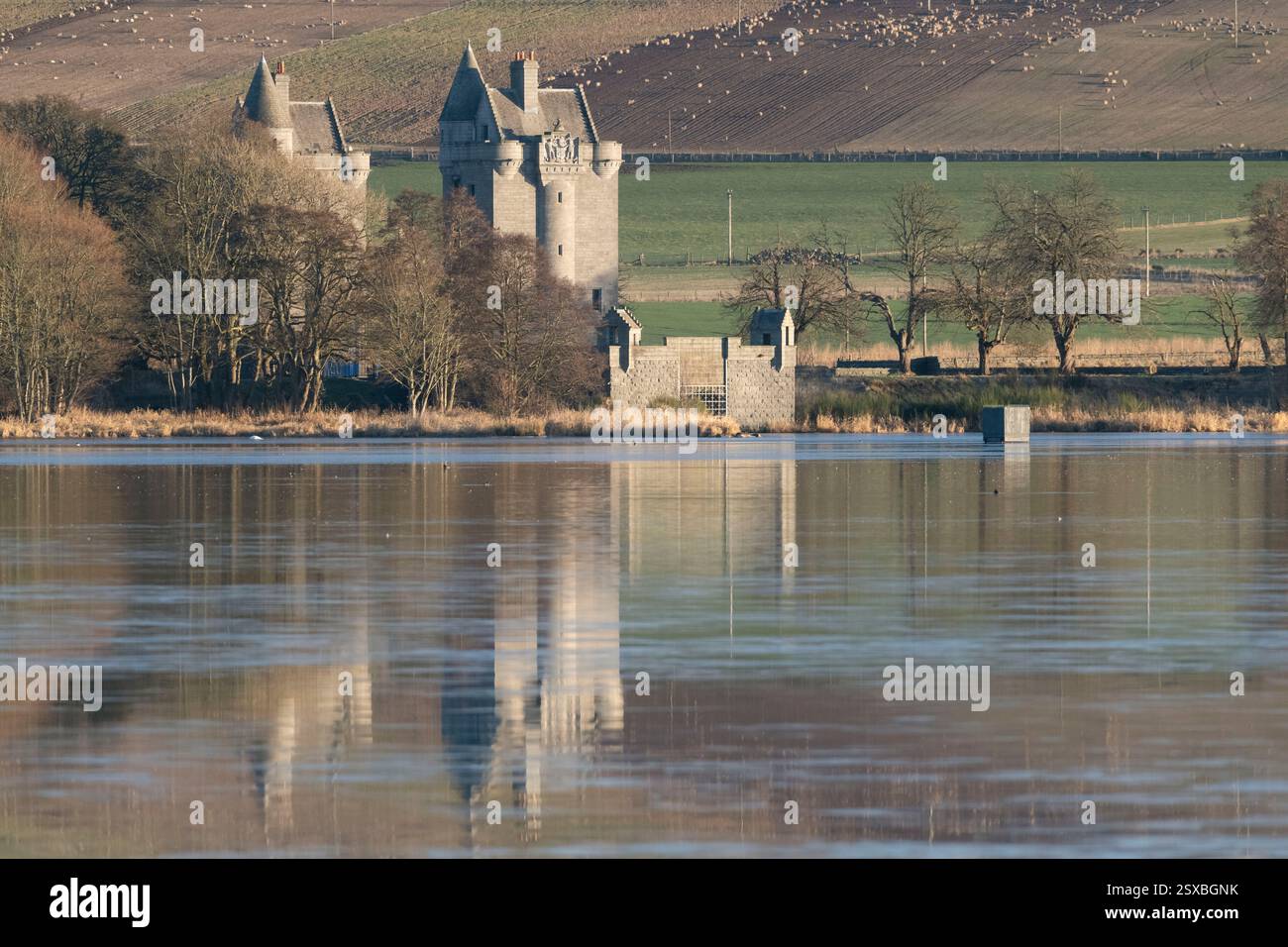 La Dunecht Estate Gate-House e la sua riflessione sulla superficie ghiacciata del lago di Skene nel primo mattino del sole in inverno Foto Stock