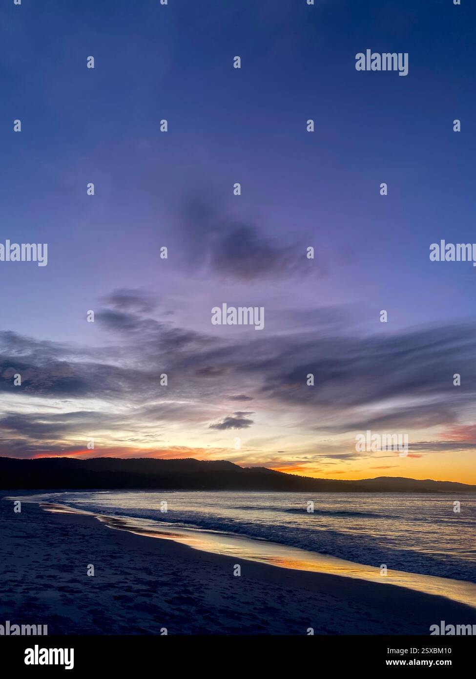 Splendido tramonto sulla costa viola sulle onde tranquille dell'oceano - cielo sereno che si riflette sulle acque calme, perfetto per viaggi, natura e fotografia paesaggistica. - Immagine stock catturata con smartphone
