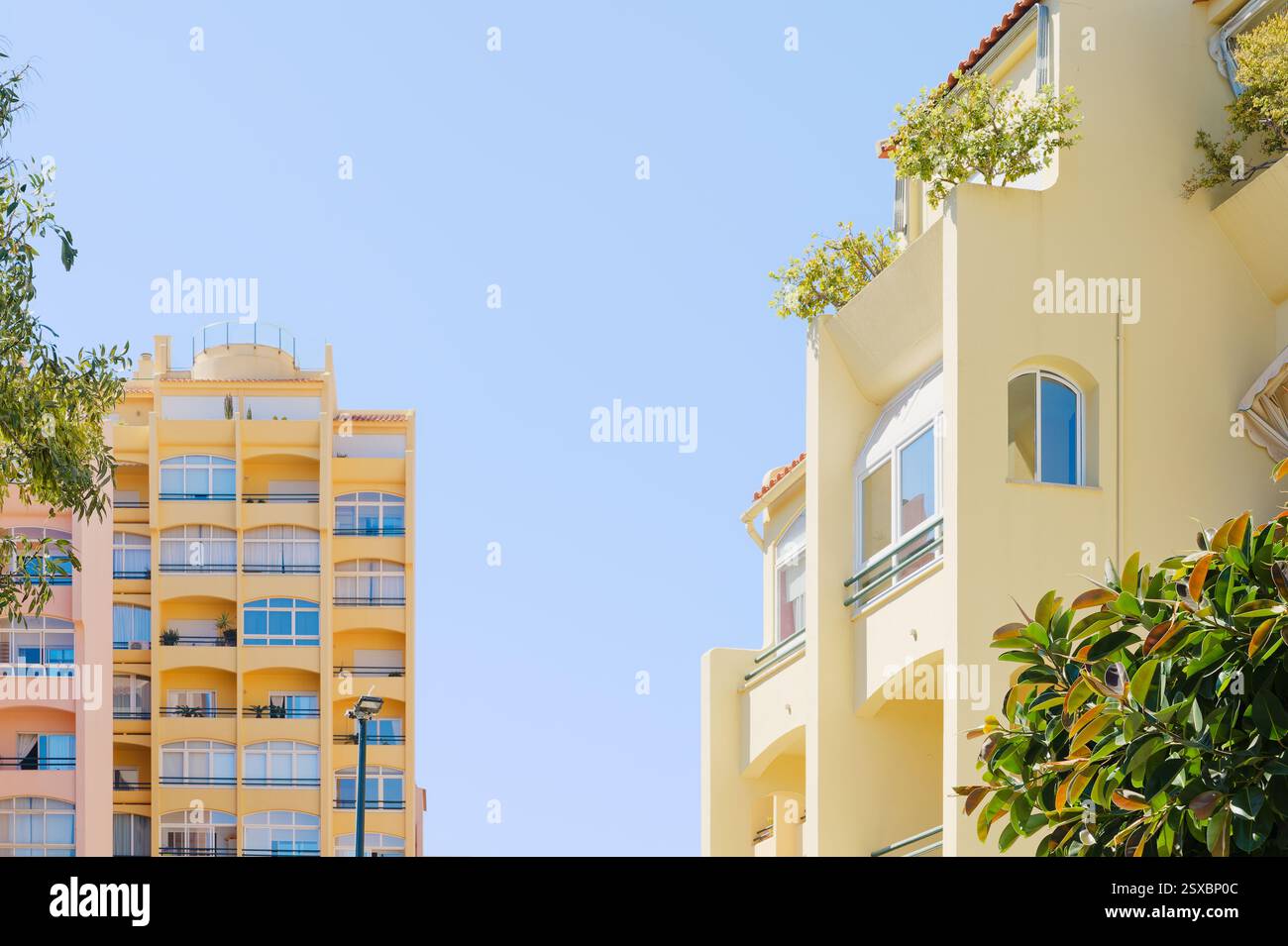 Edifici luminosi color pastello presentano eleganti balconi e lussureggiante vegetazione sul tetto contro un cielo azzurro Foto Stock