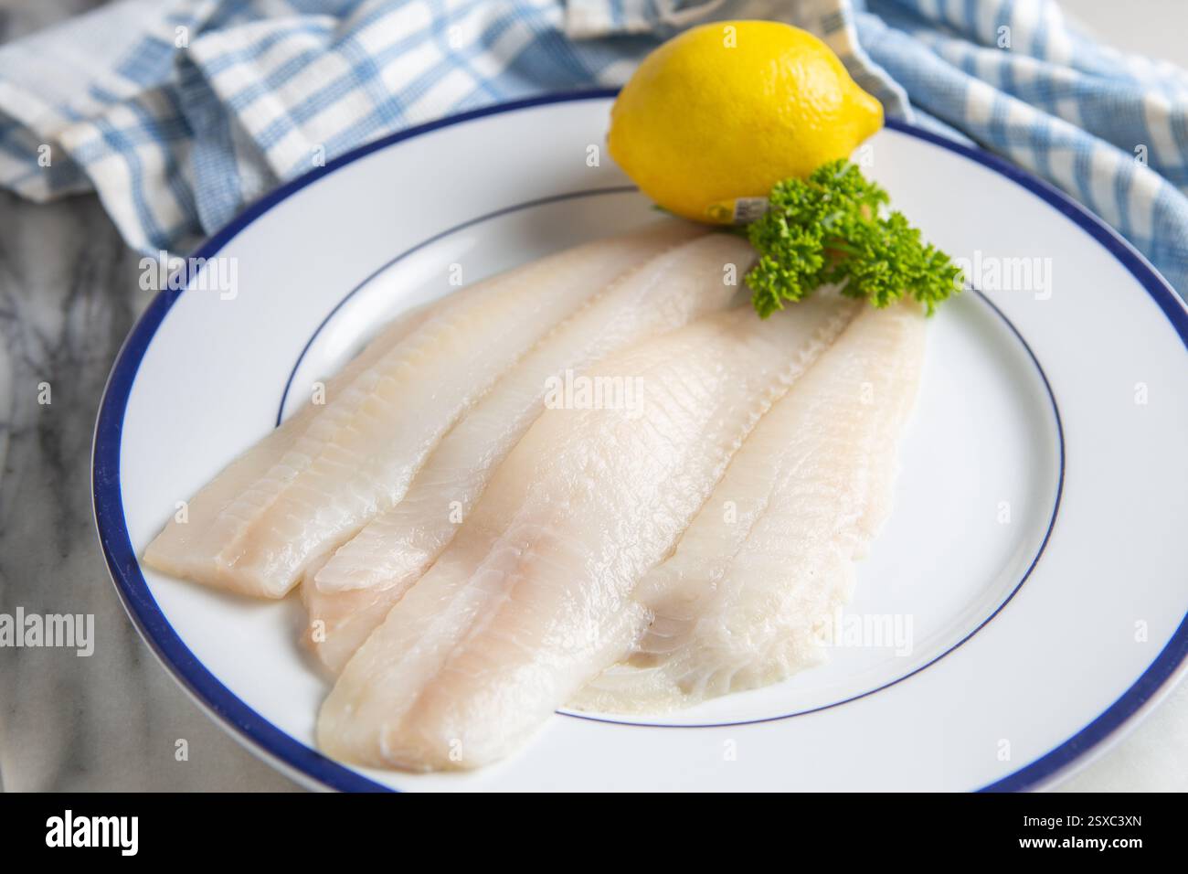 Sogliola cruda disossata, senza pelle, su un piatto con limone e prezzemolo fresco. Foto Stock