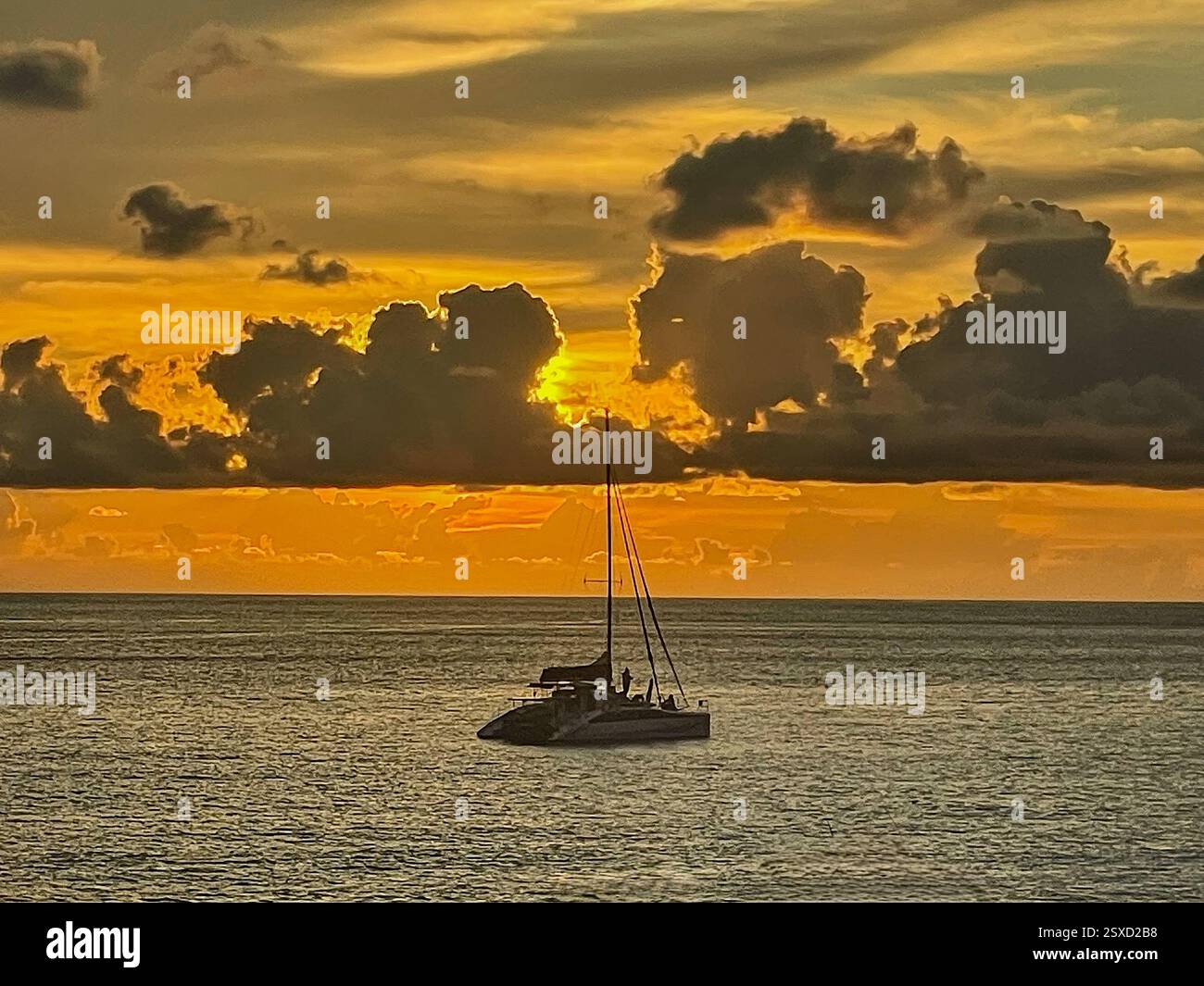 Tramonto dorato sul Mar scuro con un catamarano sull'orizzonte il sole, nascosto dietro spesse nuvole appena sopra il mare, proietta un bagliore dorato-arancione - Immagine stock catturata con smartphone