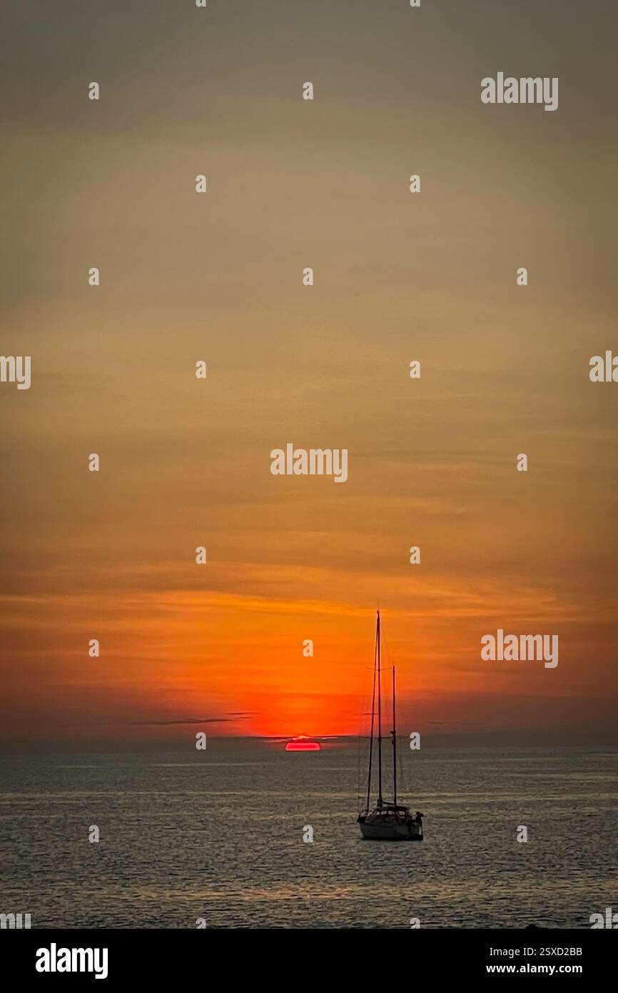 Dark Sailboat su un profondo Mare Blu sotto un tramonto infuocato Un tramonto perfetto tramonta il cielo con vibranti sfumature di arancione, giallo e rosso - Immagine stock catturata con smartphone