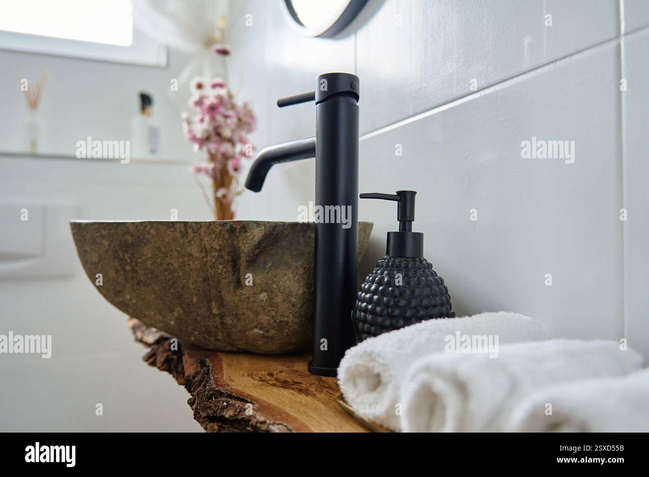 Bagno interno moderno con lavandino in pietra, rubinetto nero, asciugamani bianchi e ripiano in legno rustico. Bagno elegante con arredi in stile minimalista naturale Foto Stock
