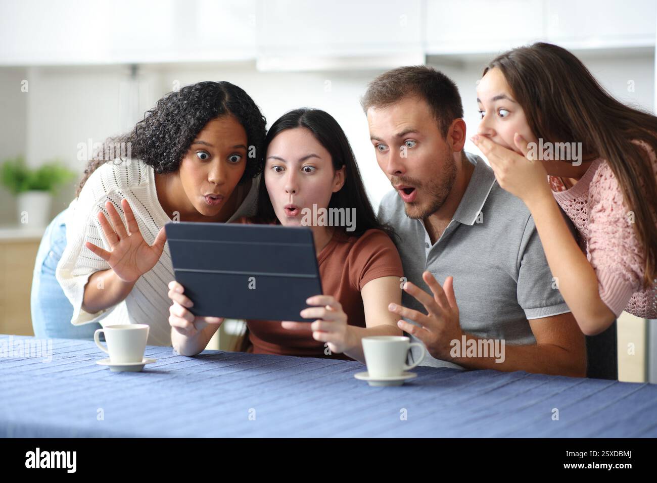 Stupito gruppo interrazziale di amici che controllano i contenuti dei tablet in cucina a casa Foto Stock
