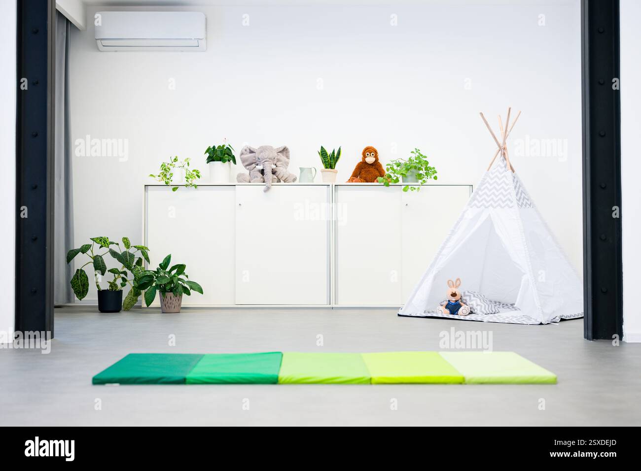 Sala giochi per bambini con tenda, giocattoli e tantissime piante per la casa. Camera per bambini dal design semplice e moderno. Foto Stock