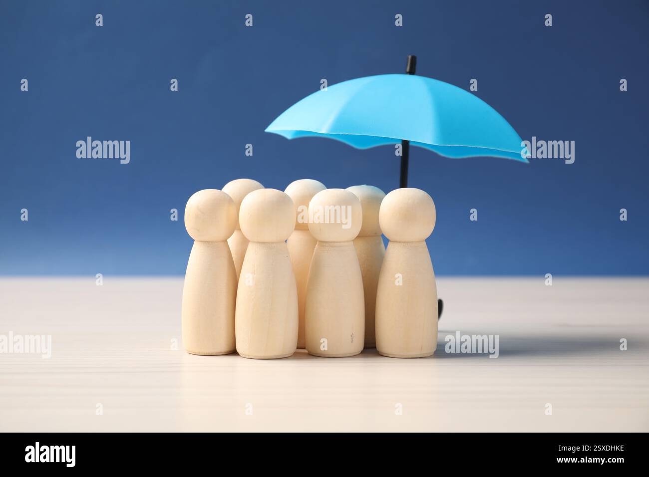 Figure umane sotto l'ombrello su un tavolo bianco su sfondo blu. Concetto assicurativo Foto Stock