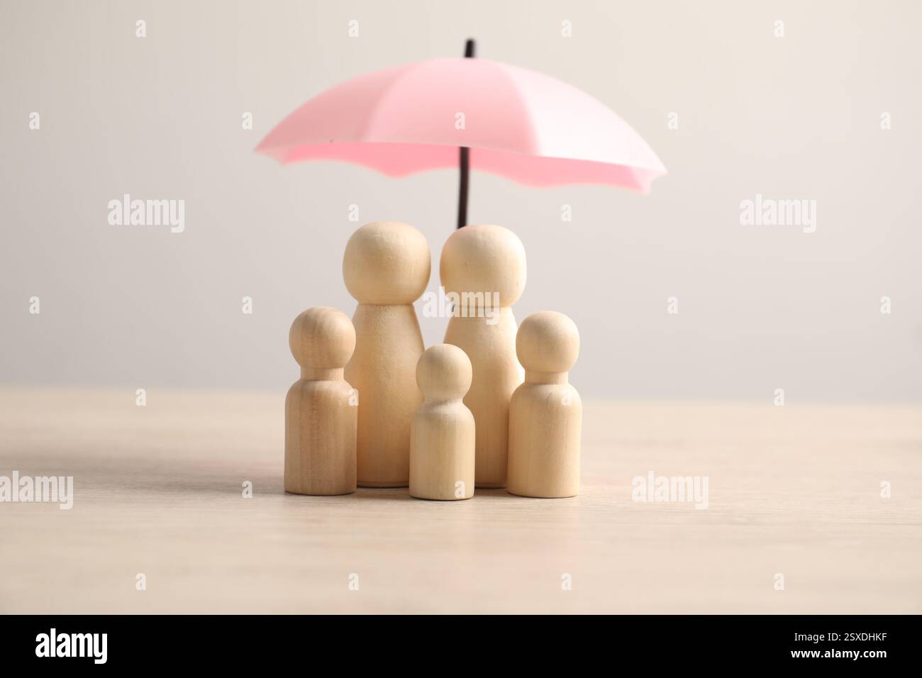 Figure umane sotto l'ombrello su un tavolo di legno chiaro. Concetto assicurativo Foto Stock