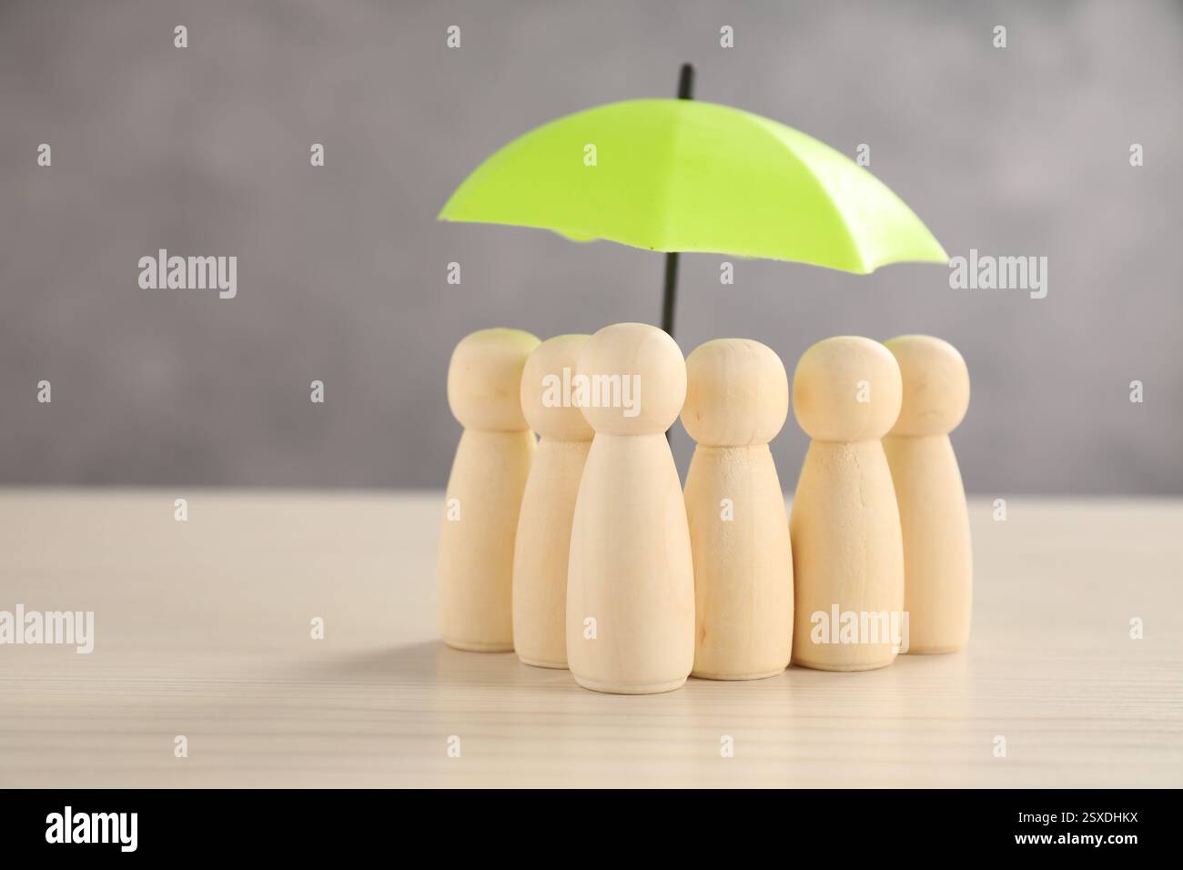 Figure umane sotto l'ombrello su un tavolo di legno chiaro. Concetto assicurativo Foto Stock