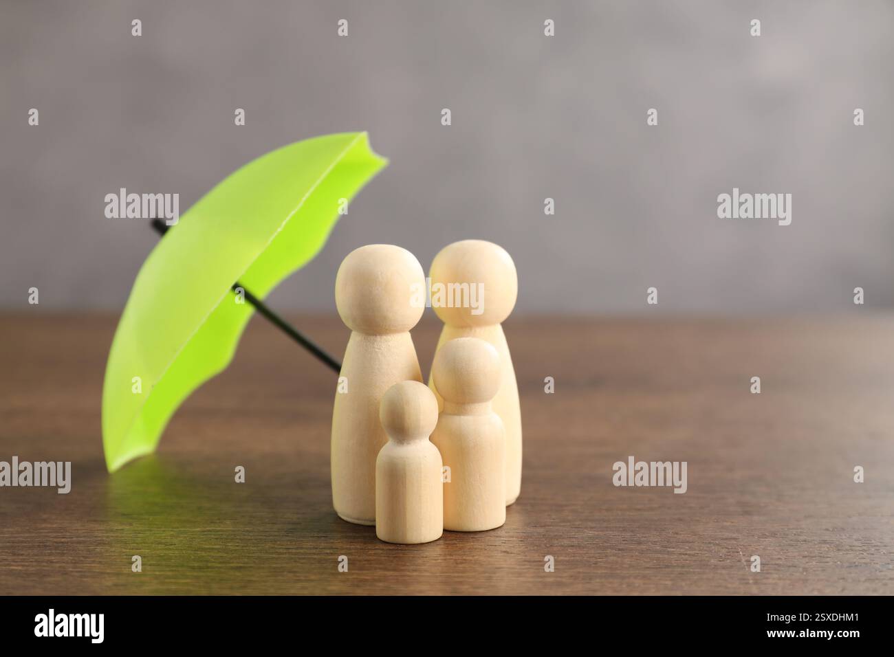 Figure umane sotto l'ombrello su un tavolo di legno. Concetto assicurativo Foto Stock
