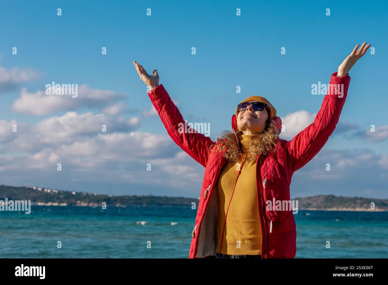 giovane donna con berretto e cuffie alzate le mani contro il mare Foto Stock