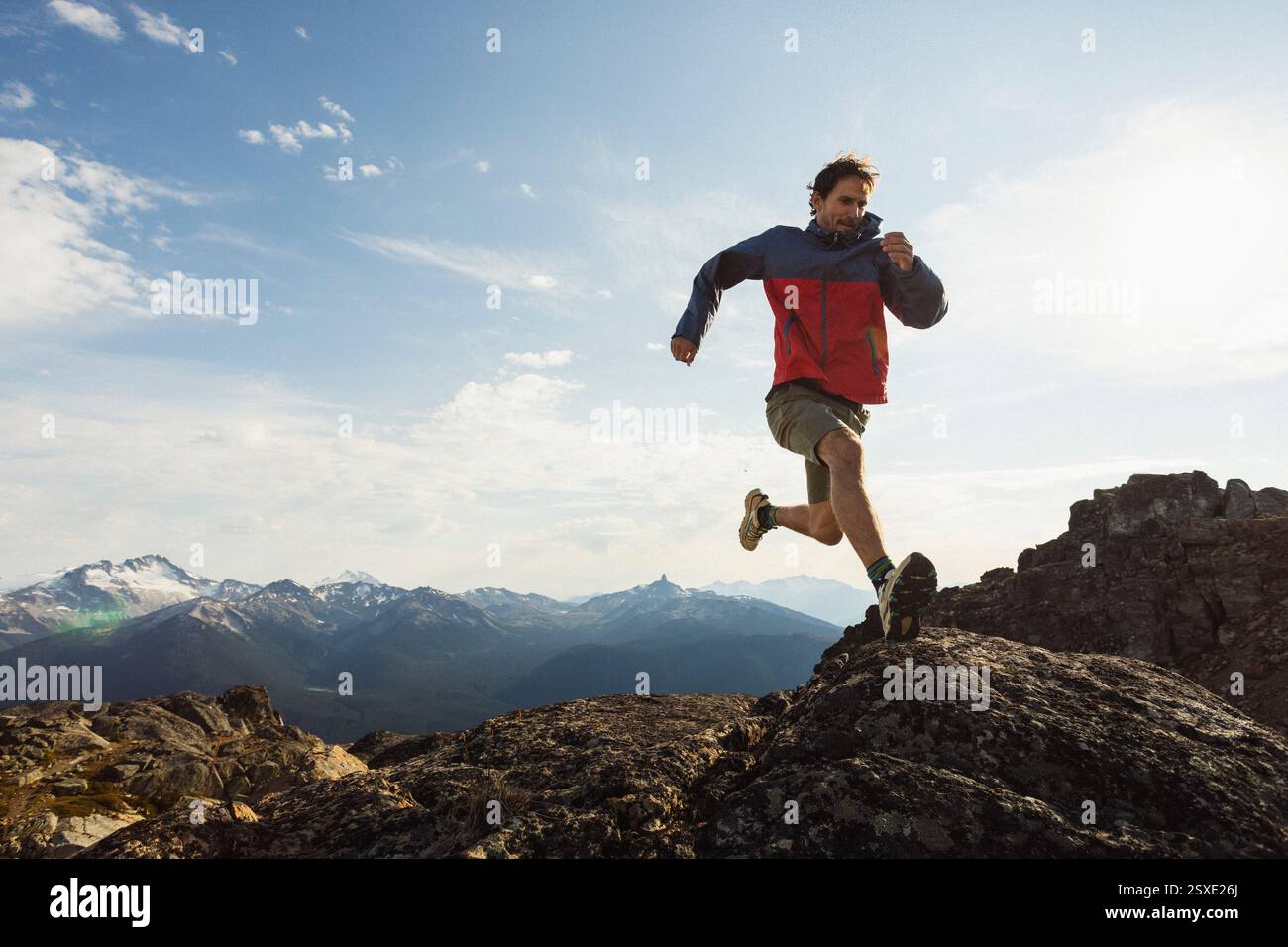 Trail runner in giacca rossa che naviga su terreni rocciosi di montagna. Foto Stock