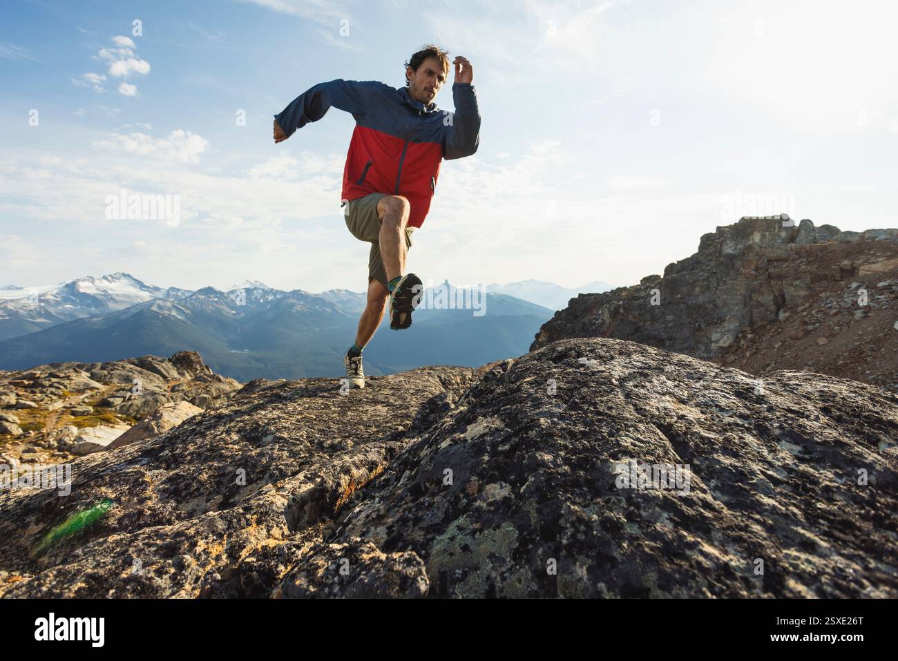 Corridore concentrato che naviga su terreni rocciosi alpini durante il giorno d'estate Foto Stock