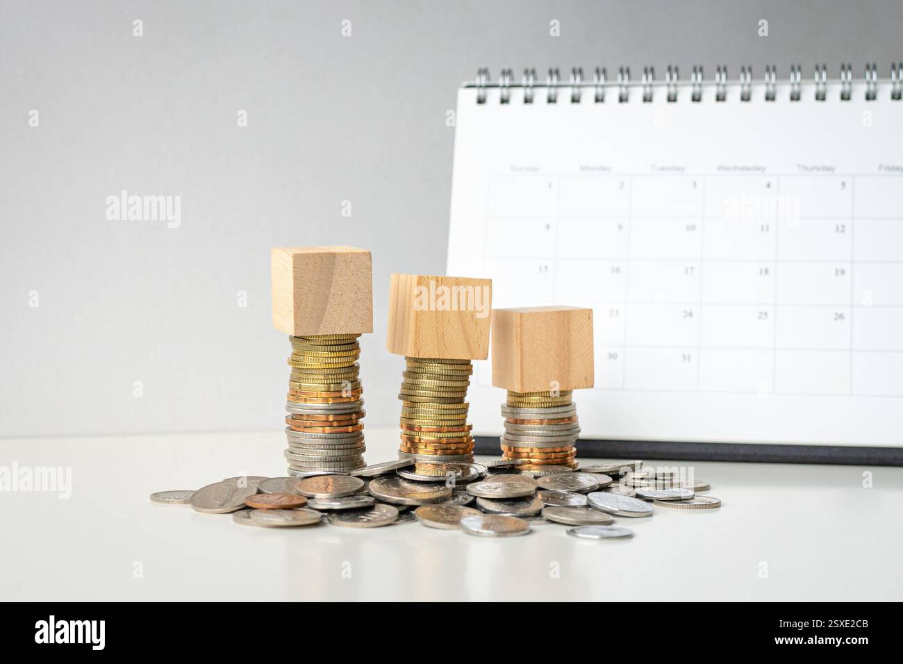 Tre blocchi di giocattoli sopra le monete, impilati e distesi sul tavolo. Tabella calendario in background. Foto Stock