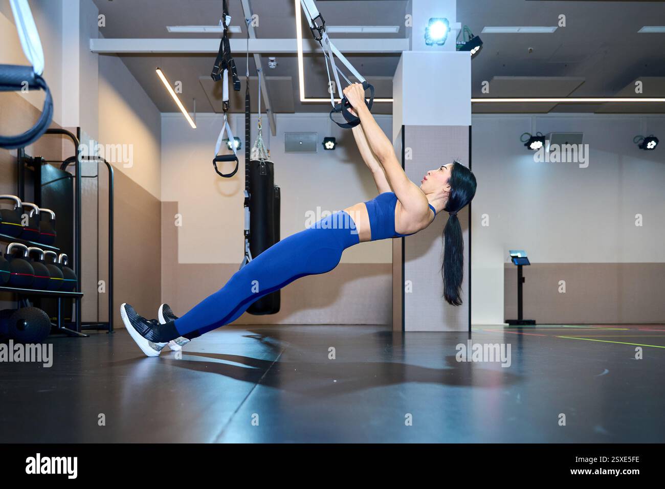 Donna atletica impegnata in esercizi di allenamento in sospensione in un ambiente spazioso e ben illuminato, concentrandosi sulla forza e sull'equilibrio Foto Stock Donna atletica impegnata in esercizi di allenamento in sospensione in un ambiente spazioso e ben illuminato, concentrandosi sulla forza e sull'equilibrio Foto Stock