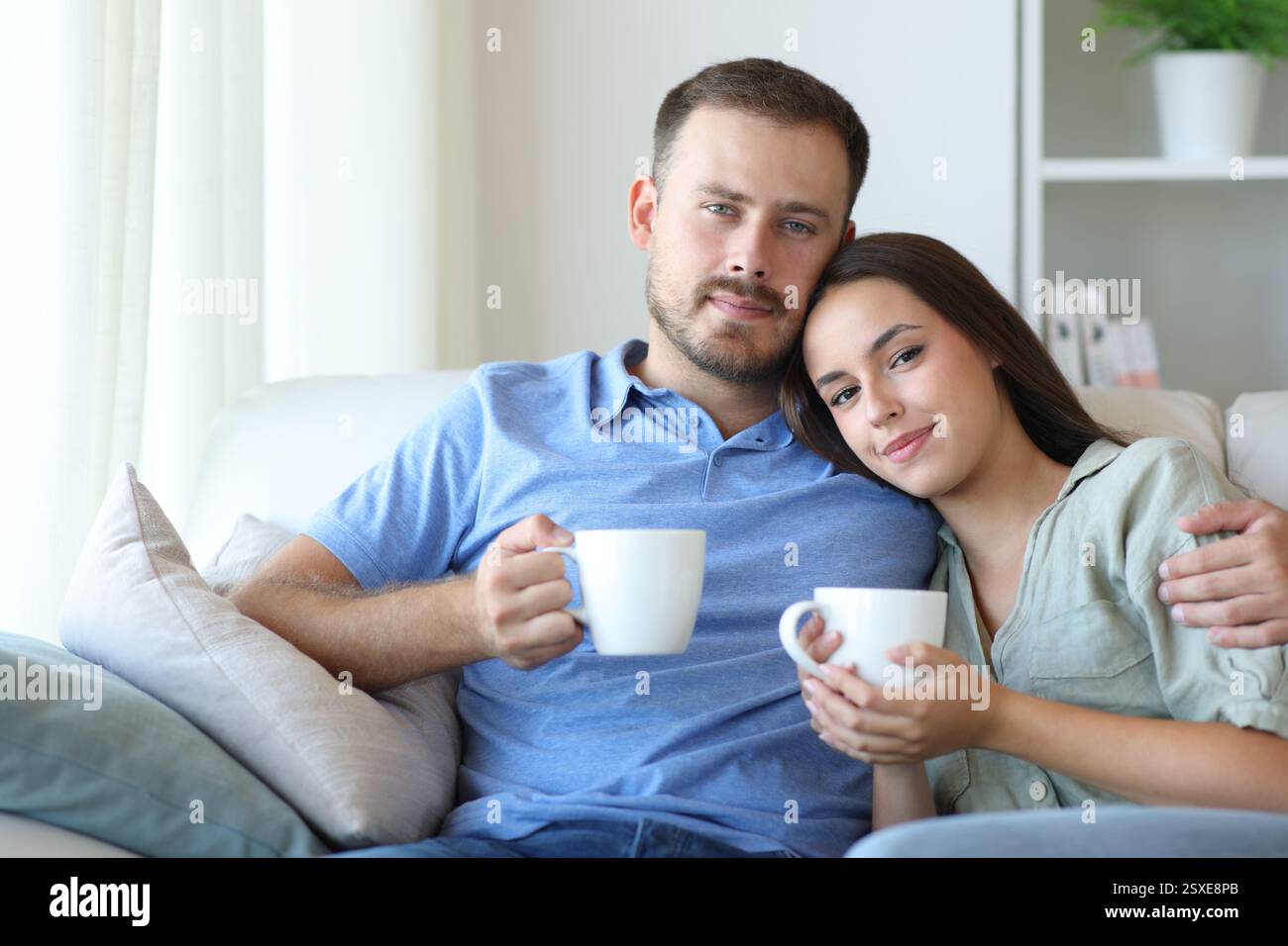 Una coppia rilassata seduto su un divano e bevendo un caffè che ti guarda a casa Foto Stock