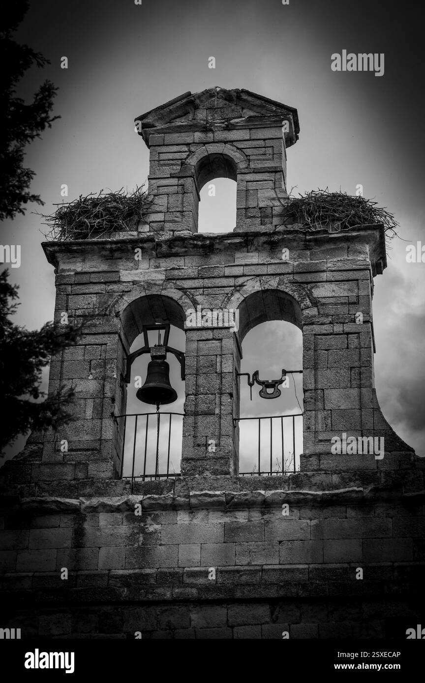 Campanile di una cappella romanica con due nidi di cicogna vuoti. Drammatico in bianco e nero Foto Stock
