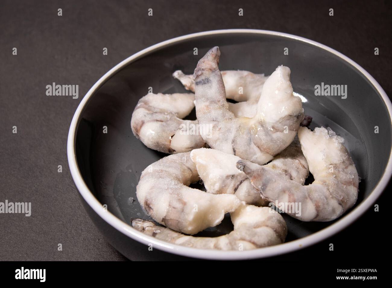 Gamberetti di tigre crudi congelati in una ciotola grigia su un tavolo da cucina grigio Foto Stock