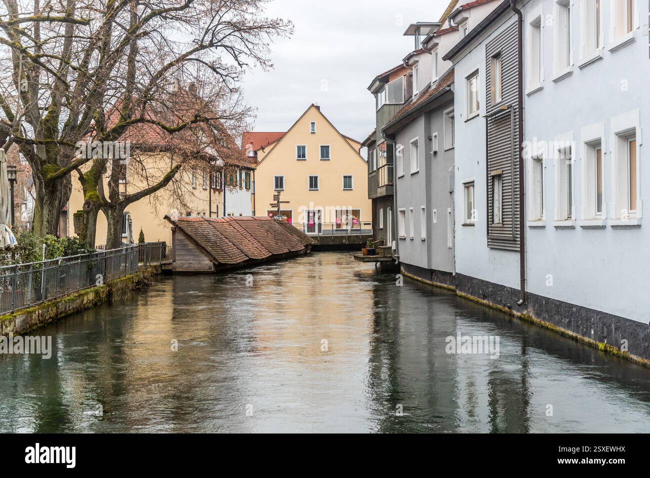 Cassette storiche per il pesce con tetti di tegole ricoperti di muschio si trovano nell'acqua del Wiesent nel centro storico di Forchheim, davanti a una casa a graticcio gialla con frontone e a una fila di case blu pallido con persiane. L'acqua calma riflette le facciate. Le cassette di legno hanno servito i pescivendoli di Forchheim per secoli per mantenere il pesce vivo, vicino all'antica Hundsbrücke. Hornschuchallee, Forchheim, Bavaria, Germania. Foto Stock