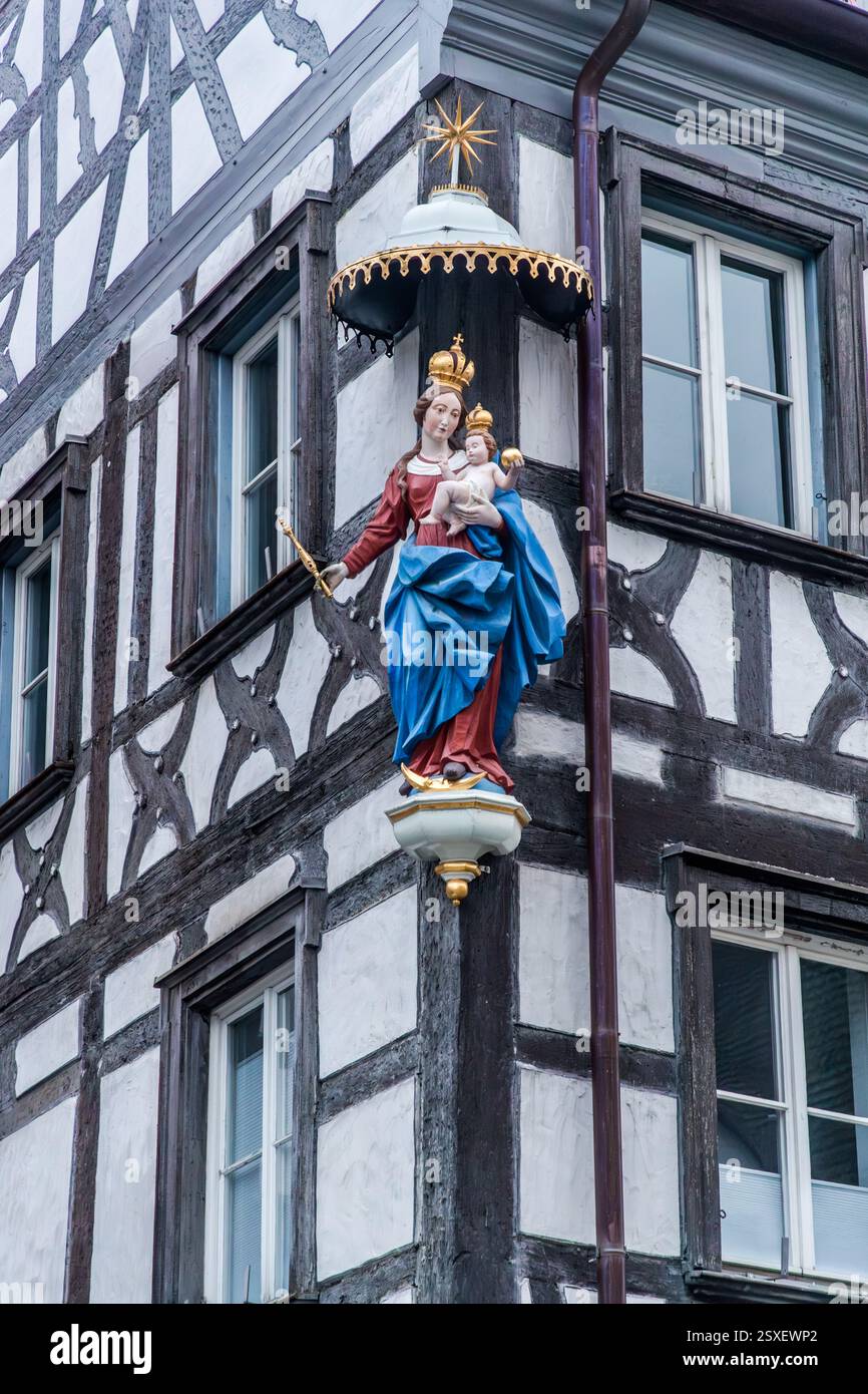 La figura della Vergine Maria con il Bambino Gesù adorna l'angolo di un edificio a graticcio bianco e nero nel centro storico di Forchheim, sotto un baldacchino dorato sormontato da una stella dorata. Quattro file di finestre si estendono a destra della figura, e un tetto di tegole rosse con abbaini corona l'edificio. St.-Martin-Straße, Forchheim, Bavaria, Germania. Foto Stock