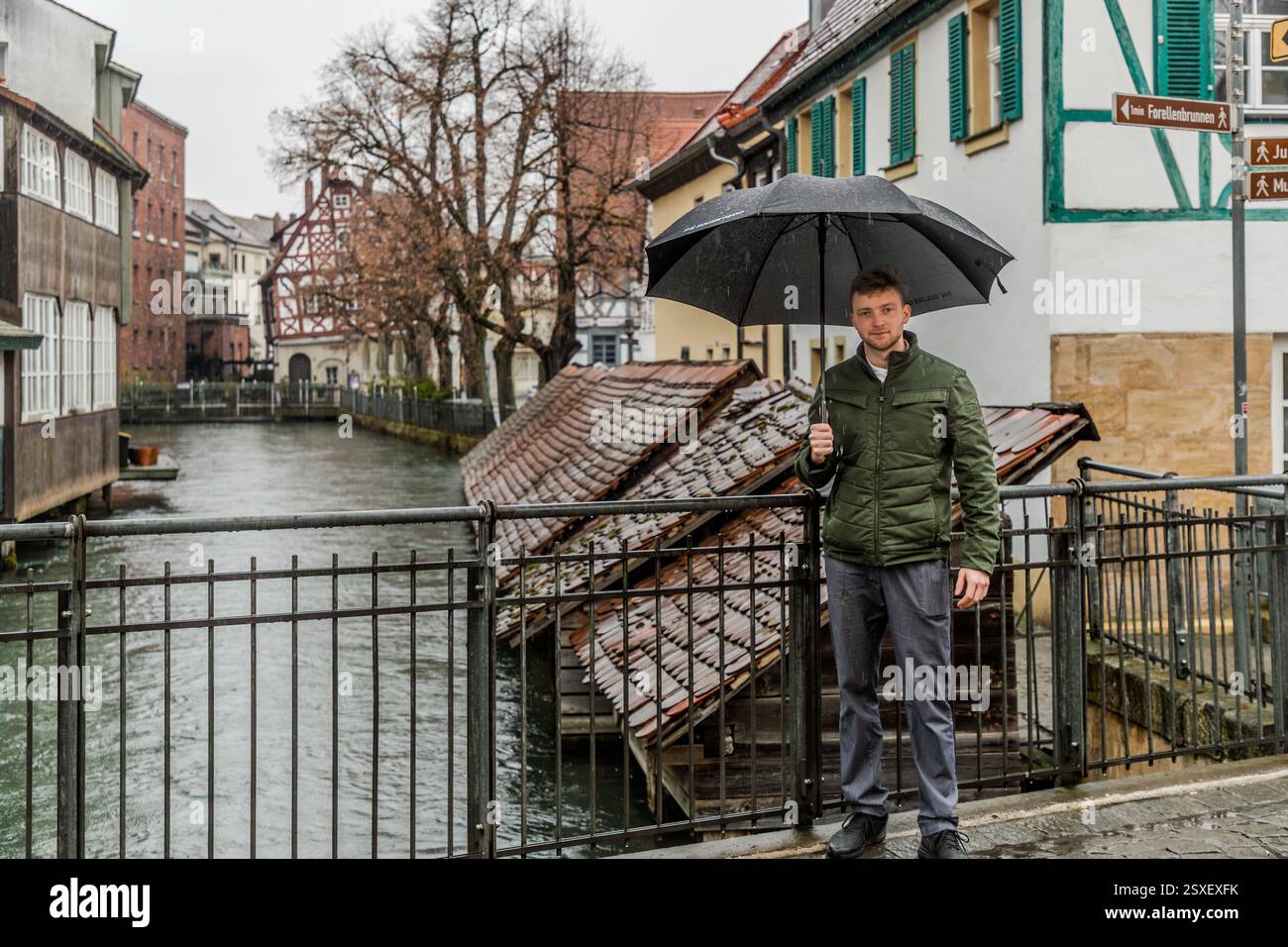 Anton Karnbaum si trova sotto un ombrello e osserva la carpa nell'acqua che scorre sotto le capanne dei pesci. Forchheim, Baviera, Germania Una persona in Germania tiene un ombrello in una giornata di pioggia vicino a un canale. Foto Stock