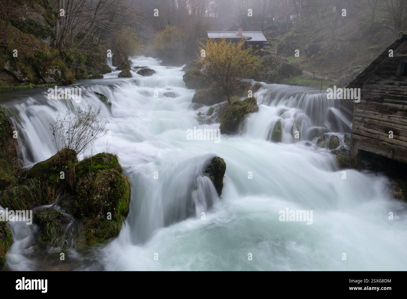 Cascate sul fiume Krupa con mulini ad acqua in legno, la nebbia sorge dal fiume turbolento, mattinata tranquilla Foto Stock