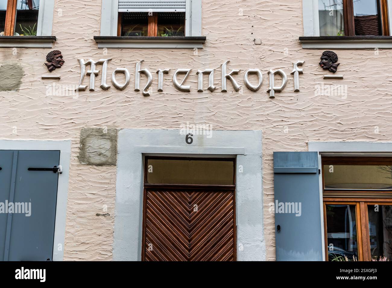 La scritta "Mohrenkopf" in caratteri gotici decora la facciata di un edificio in Wasserturmstraße a Erlangen, Baviera, Germania, affiancata da due rilievi di teste color bronzo. Secondo l'archivio cittadino di Erlangen, il nome appartiene a un gruppo di nomi storici di case e locande della città che sono oggetto di un dibattito pubblico sulla cultura della memoria di Erlangen a causa della componente razzialmente carica del termine – come nel caso della farmacia "Mohren-Apotheke" e della ex locanda "Mohrenkopf" in Schiffstraße. Foto Stock