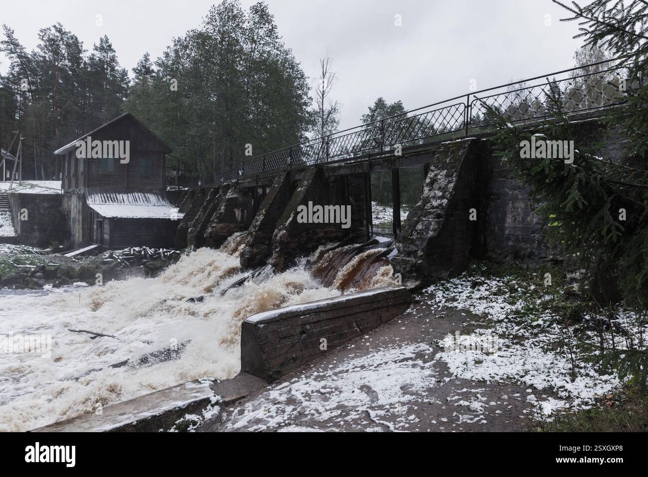 Un mulino ad acqua in legno situato accanto ad un ruscello che scorre veloce sotto un paesaggio innevato, evocando fredda serenità invernale. Sosnovskaya Hydroelectric Power S Foto Stock
