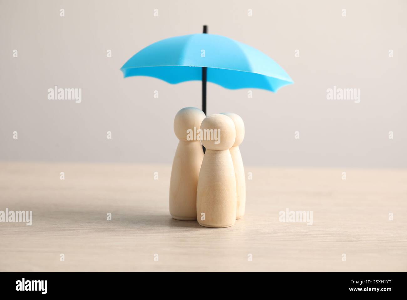 Figure umane sotto l'ombrello su un tavolo di legno chiaro. Concetto assicurativo Foto Stock