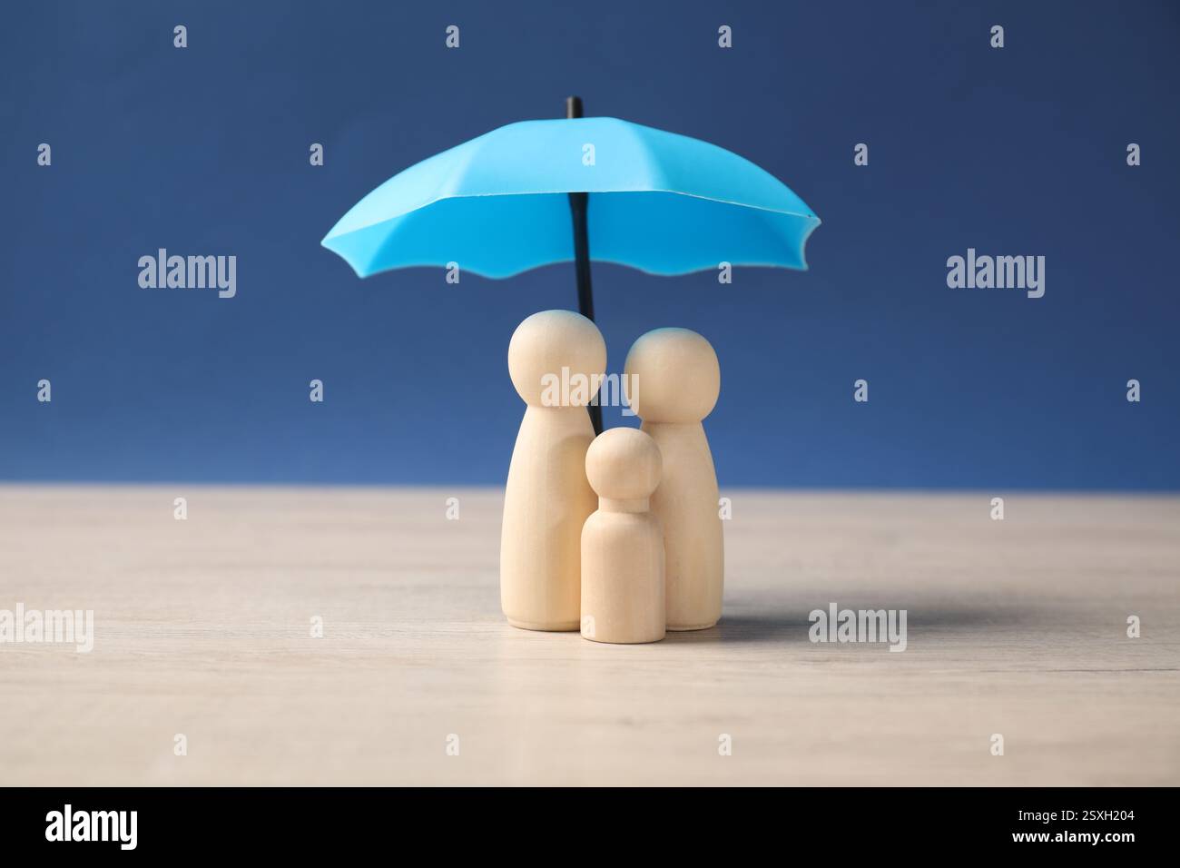 Figure umane sotto l'ombrello su un tavolo di legno chiaro su sfondo blu. Concetto assicurativo Foto Stock
