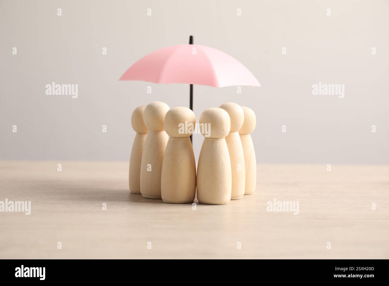 Figure umane sotto l'ombrello su un tavolo di legno chiaro. Concetto assicurativo Foto Stock