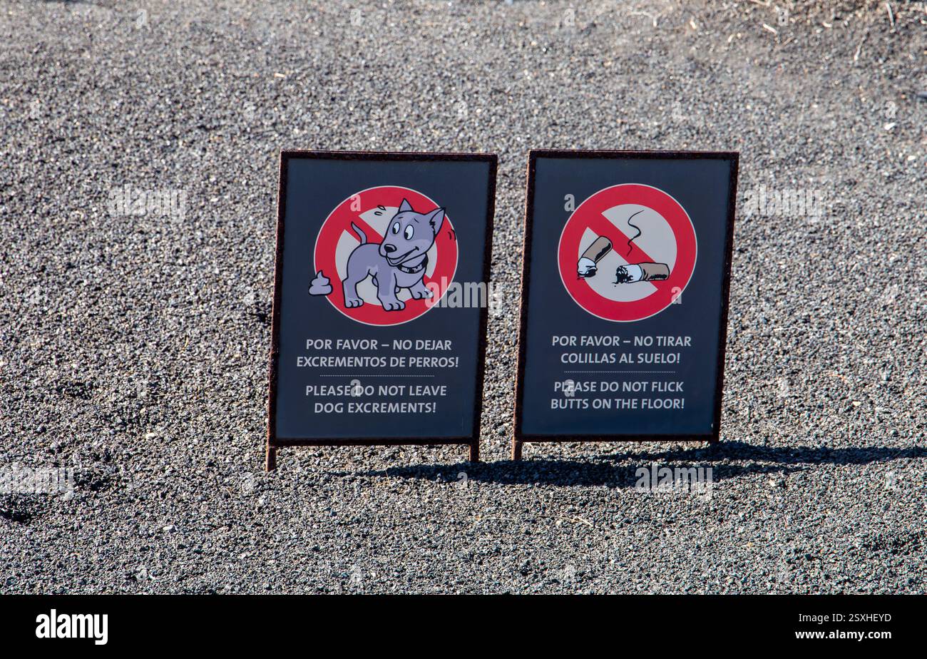 Cartelli bilingue che invitano a non lasciare escrementi di cane o mozziconi di sigaretta a terra su un sentiero di ghiaia a Costa Teguise Lanzarote Foto Stock