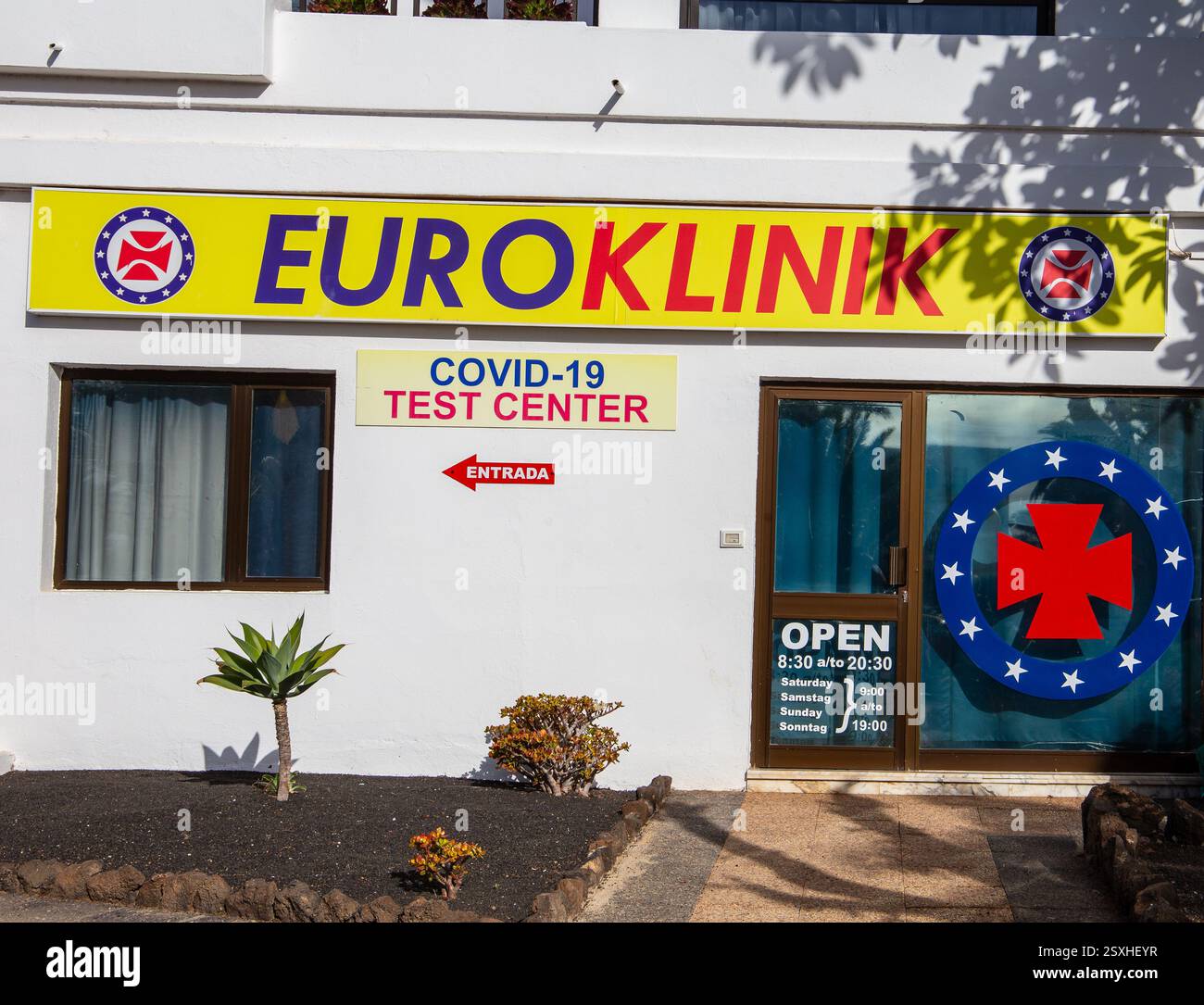 Vista esterna del centro di test Euroklinik COVID-19 con cartello di ingresso e simbolo di emergenza su un edificio per uffici Foto Stock