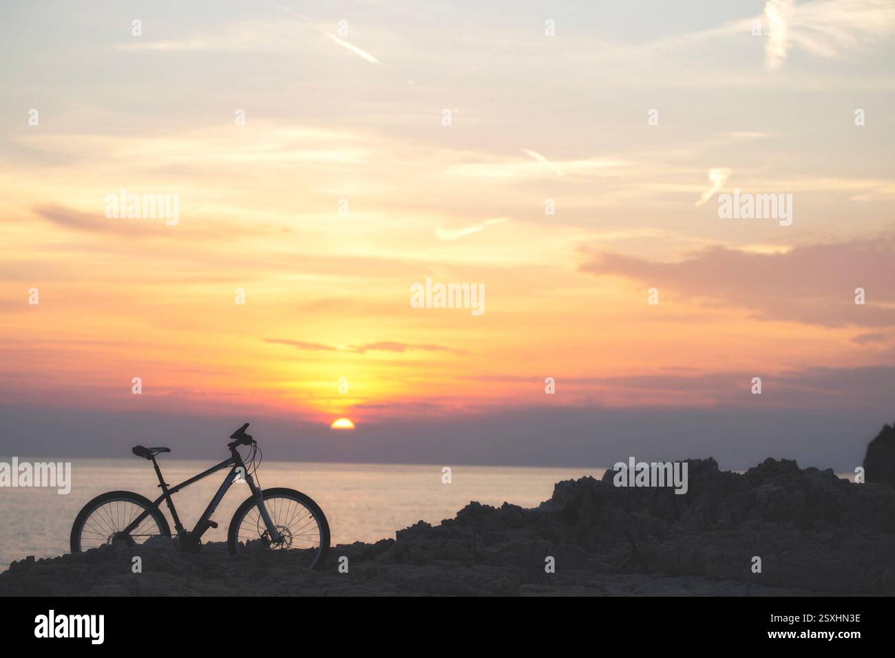 bicicletta retroilluminata sul mare roccioso al tramonto, viaggio all'orizzonte Foto Stock