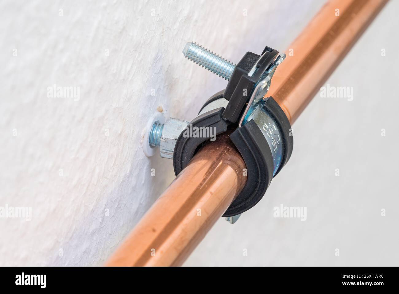 Un primo piano dettagliato di un tubo in rame fissato a una parete bianca utilizzando un morsetto a staffa in metallo e plastica. Foto Stock