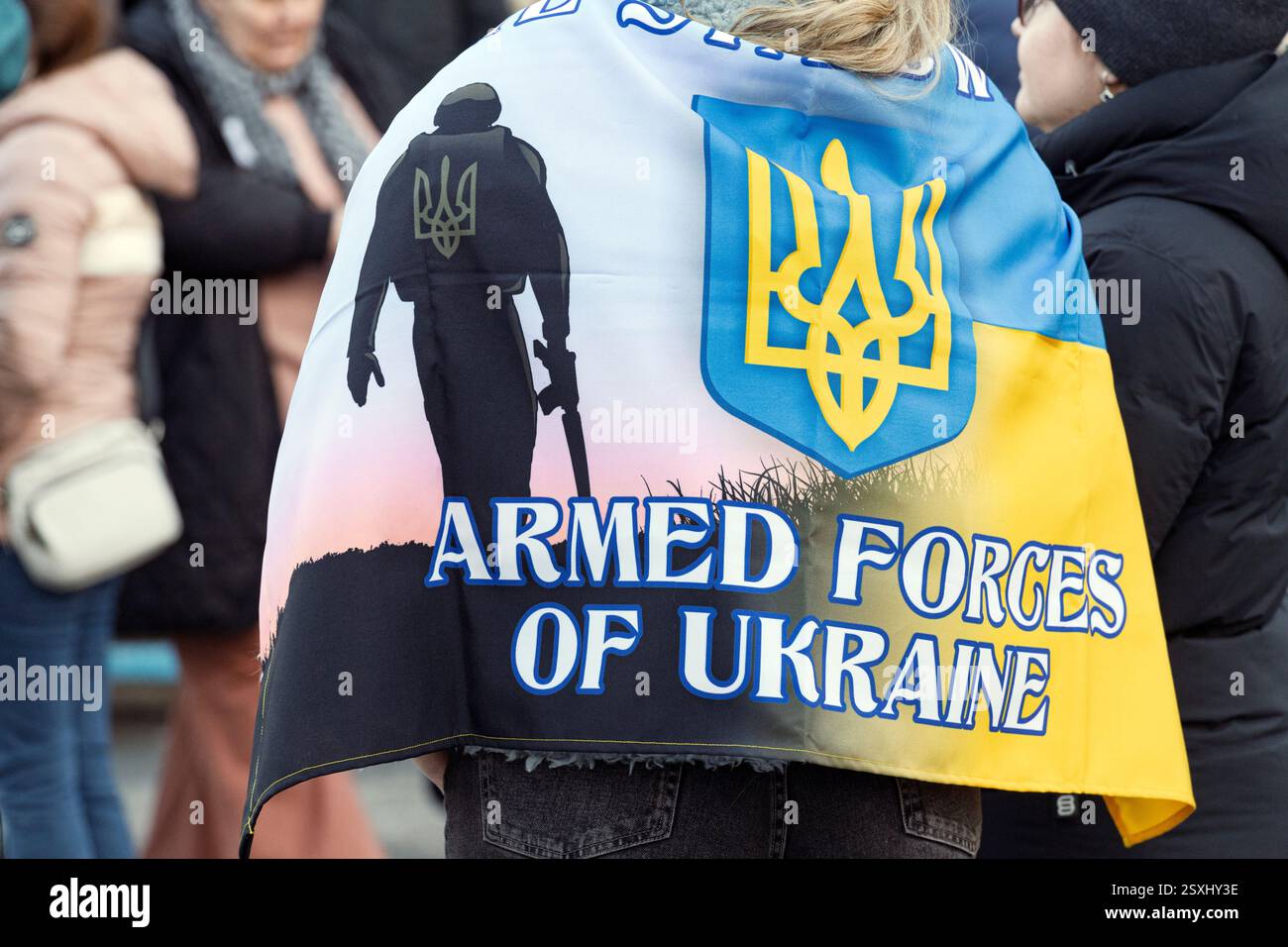 Persona che indossa una bandiera con l'emblema delle forze armate ucraine e la silhouette di un soldato presso la piazza municipale di Calgary, 23 febbraio 2025 Foto Stock