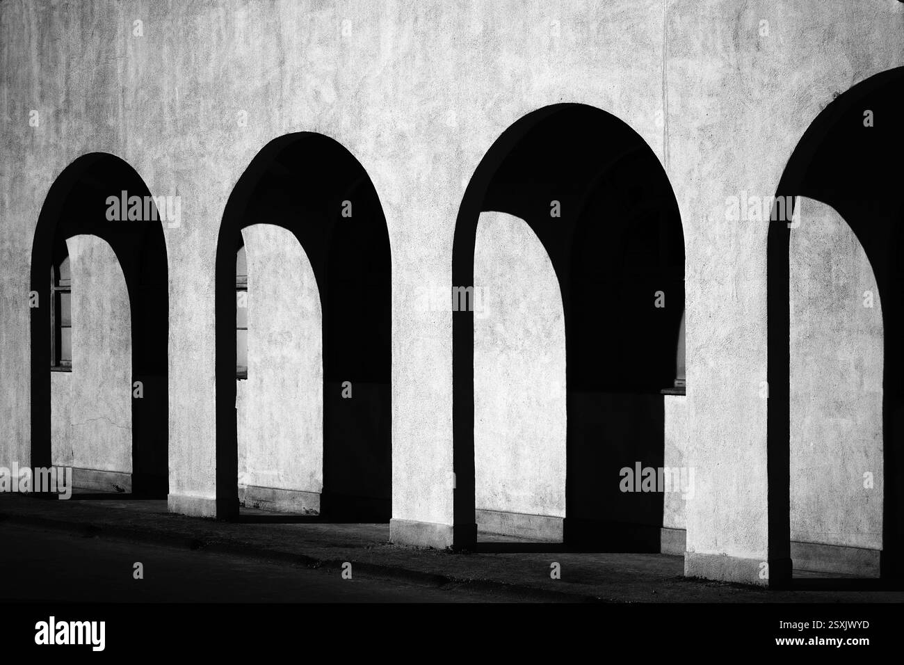 Spazio liminale bianco e nero fotografie architettoniche di fine arte che mostrano pattern ripetuti di luce e ombre attraverso il corridoio esterno ad arco di Foto Stock