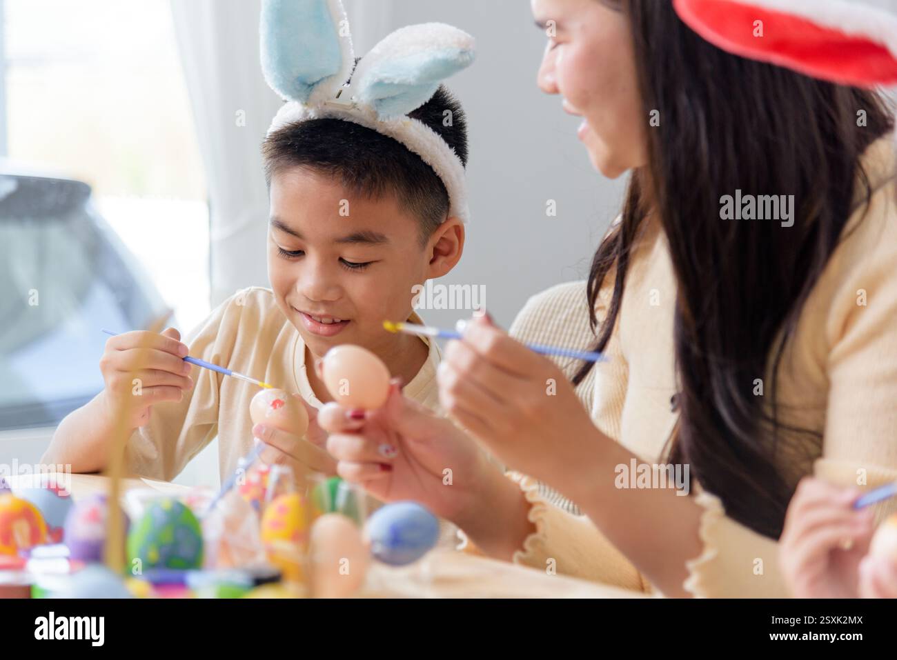 Felicità di Pasqua. Una madre e i bambini amano dipingere insieme le uova di Pasqua a un tavolo festivo, festeggiando la vacanza con divertimento e creatività. Pasqua da Foto Stock