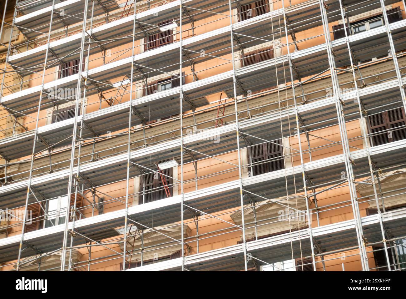 Facciata dell'edificio coperta da impalcature metalliche durante i lavori di ristrutturazione e sviluppo di proprietà, evidenziando motivi geometrici e dettagli architettonici classici con esterno arancione Foto Stock